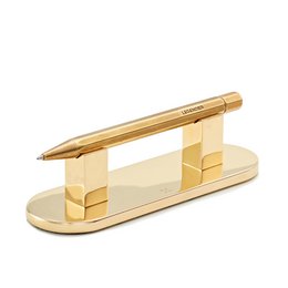 Brass pen stand with a sleek, minimalist design. Features a rectangular base with a raised pen holder in the center. Suitable for use as a desk organizer or decorative accent.