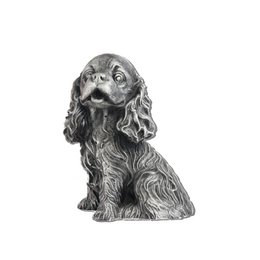 A silver-colored Cocker Spaniel figurine, sitting on a wicker chair against a background of lush greenery.
The silver-colored Cocker Spaniel figurine has a detailed, realistic design with a curly, textured coat. The dog is sitting upright on a wicker chair, surrounded by lush, green foliage. The figurine captures the breed's friendly and attentive expression.
