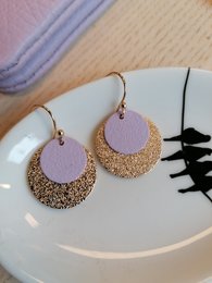 Elegant statement earrings featuring a lilac-colored disc with a glittering gold-toned halo. The unique design adds a touch of glamour to any outfit.
