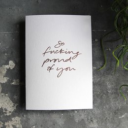 A hand-foiled greeting card with the text "So fucking proud of you" in cursive script.