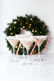 Elegant martini glasses filled with festive cocktail, garnished with candy canes, set against a blurred Christmas tree background.