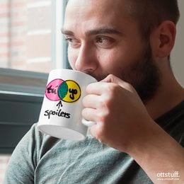 A white ceramic mug with a colorful "You, me, spoilers" graphic design. The mug features a playful, pop art-inspired illustration of two people and a speech bubble.