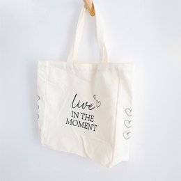 White cotton tote bag with "Live in the moment" text and heart icons printed on it. Suitable for casual everyday use or as a reusable shopping bag.