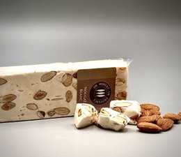 A rectangular white nougat candy bar weighing 100g, packaged in a beige wrapper with a blue logo and text.