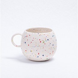  A white ceramic mug with a speckled pattern, featuring a round, tall shape and a handle. The mug is suitable for parties and events.