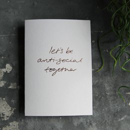 A hand-foiled greeting card with the text "Let's be anti-social together" written in a cursive font.