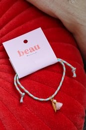 A delicate, adjustable anklet with a simple, elegant design. The anklet features a white tag with the word "Beau" printed on it, and the anklet itself is made of thin, white cords tied together in a minimalist style.