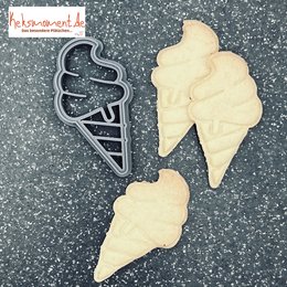 Cream-colored ice cream cone-shaped cookie cutter on a glittery background.