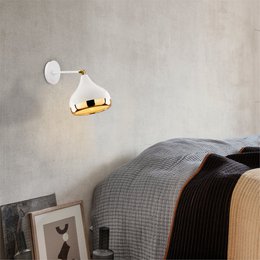  A modern, minimalist wall lamp with a round, metallic shade in a neutral color palette, suitable for illuminating a bedroom or living space.