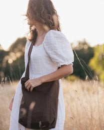A brown canvas shoulder bag with a simple, minimalist design. The bag features a rectangular shape, a single strap, and a neutral brown color that complements a variety of outfits.