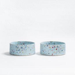  Two round, soft blue pet bowls made of stoneware with colorful speckled patterns.