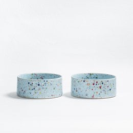 Two round, soft blue pet bowls made of stoneware with colorful speckled patterns.