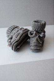  Gray hand-knitted merino wool baby shoes with bow detail.