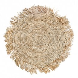 Round natural raffia placemat with fringed edges, suitable for use in dining or home decor.