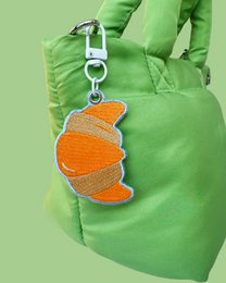 Orange croissant-shaped bag charm keyring with metal clasp, bright green nylon bag accessory.