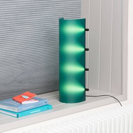 A tall, cylindrical table lamp with a dark green, gradient design. The lamp has a modern, minimalist style and appears to be made of metal or a similar durable material.