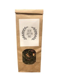 A loose leaf tea blend in a kraft paper bag with a floral wreath design and the text "Dear Miss Tea" printed on it. The tea appears to be a mix of dried leaves and flowers.