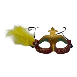 Orange rød maske med grønne vipper og en gul fjer