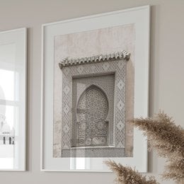 The image shows an ornate architectural detail, likely from a building in a Middle Eastern or North African style. The focal point is a decorative arched doorway or window frame, featuring intricate geometric patterns and ornamental elements. The overall style suggests a traditional Islamic or Moorish architectural influence.