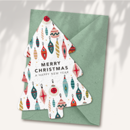  A Christmas card featuring a Christmas tree design with various ornaments and decorations, including balls, stars, and other festive elements. The card is printed on seed paper, making it an eco-friendly and sustainable option. The card has a green envelope.