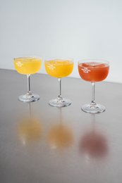 Elegant cocktail coupe glasses in various colors, including amber, orange, and red. The glasses have a classic, stemmed design suitable for serving cocktails or mocktails.