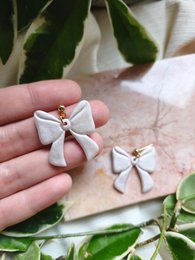  Elegant bow-shaped earrings crafted from lustrous mother of pearl, available in gold and silver finishes. Versatile statement accessory for any occasion.