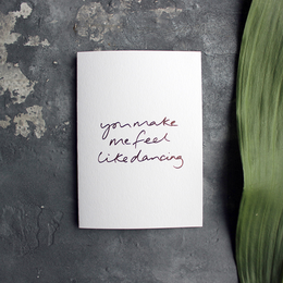 A hand-foiled greetings card with the text "You make me feel like dancing" written in cursive script. The card appears to be part of a love or romantic-themed collection.