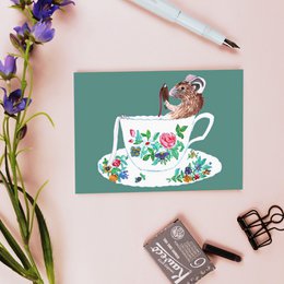 A colorful postcard featuring a teacup with a mouse illustration and floral designs, perfect for sending to friends or displaying as home decor.