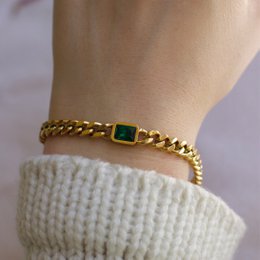 Gold-toned Cuban link chain bracelet with green gemstone accent.