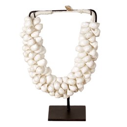 A necklace made of small white shell beads arranged in a layered, clustered design. The necklace has a metal frame and is displayed on a black stand.