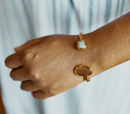 Elegant gold-toned bangle bracelet with a small turquoise-colored stone accent. Delicate and stylish accessory.