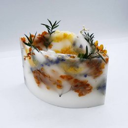 Large oval April shade candle with vibrant colors including rojo, amarillo, azul claro, salmón, and violeta. Candle features natural floral and botanical elements embedded within the wax.