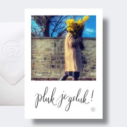 A colorful, artistic image of a person standing in front of a brick wall, with the text "Pluk je geluk!" which means "Pluck your luck!" in Dutch. The image has a vintage, polaroid-style aesthetic.