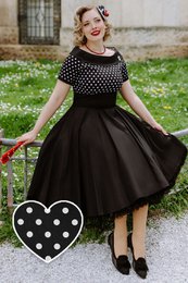  A black and white polka dot 1950s style swing dress with a fitted bodice, off-the-shoulder neckline, and a full, flared skirt. The dress features a classic retro design with a timeless polka dot pattern.