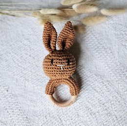 Handmade crochet rabbit rattle in neutral sand color, designed as a baby teether with textured surface and rabbit ears.
