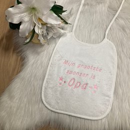  "Soft, white baby bib with the text 'Mijn grootste sponsor is Opa' (My biggest sponsor is Grandpa) printed on it. The bib has a simple, minimalist design with stars around the text."

This baby bib has a soft, white fabric material. The text "Mijn grootste sponsor is Opa" (My biggest sponsor is Grandpa) is printed on the bib in a simple, minimalist style with stars surrounding the text. The design and text on the bib suggest it is intended as a gift or keepsake for a grandparent.