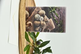 Pack of greeting cards nr63 featuring a close-up image of quail eggs nestled in a woven basket on a wooden surface, surrounded by green leaves.
