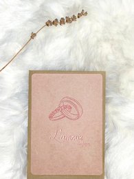Two gold wedding rings on a pink card with the text "I do" printed on it.