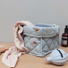 A quilted, padded storage basket in a light blue color with a dinosaur print pattern. The basket has a flap closure and appears to be made of a soft, plush material.