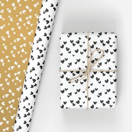 Rolls of wrapping paper with a repeating heart pattern in gold and pink colors. The paper comes in various color combinations including rose/gold, black/white, gold/white, gold/rose, black/white/champagne, champagne/white, and kraft/white. The paper has a stylish and festive design suitable for gift wrapping.