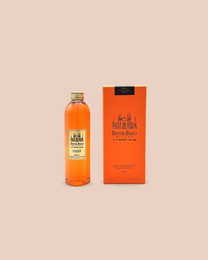 A reed diffuser with a glass bottle filled with an orange-colored liquid. The bottle has a white cap and is placed on a wooden surface against an orange background.