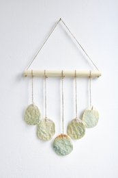 Bohemian wall hanger made of ceramic, featuring round, textured discs in neutral tones suspended from a wooden frame.