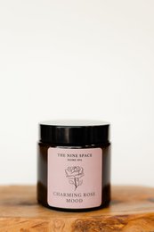 A tall, round, pink-colored scented candle in a glass jar with a black lid, presented in a green-colored box.