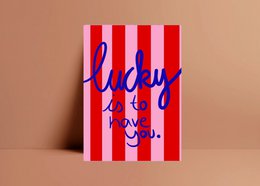 A colorful postcard with the text "Lucky to have you" written in a cursive font against a striped red and white background.
