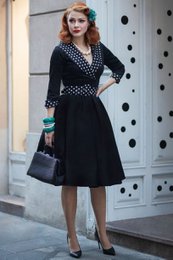  A black and white polka dot dress with a fitted bodice and a flared skirt. The dress has a v-neck and 3/4 length sleeves. The dress appears to be made of a structured fabric and has a retro, 1950s-inspired style.