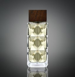 Tall, rectangular glass bottle with a wooden cap, containing a light-colored liquid. The bottle has a geometric diamond pattern design.