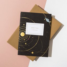 A greeting card with a starry night sky design and the text "Written in the Stars" printed on the front. The card comes in a harvest-colored envelope.
