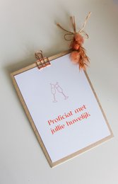  A white wedding card with a decorative orange feather attached to a wooden clip. The card has the text "Please save our date" printed on it.