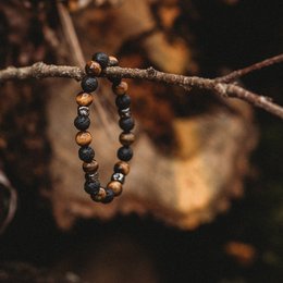 A bracelet made of dark-colored beads, possibly representing a transformation or change. The bracelet is hanging from a branch in a natural, earthy setting with a lit candle nearby.