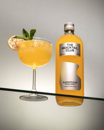Mocktail Blossom Bliss 99cl, a vibrant orange non-alcoholic beverage with a fresh citrus flavor and a garnish of mint leaves.